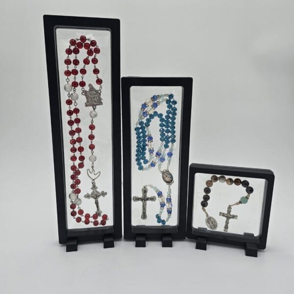 Three floating display cases holding keepsake rosaries