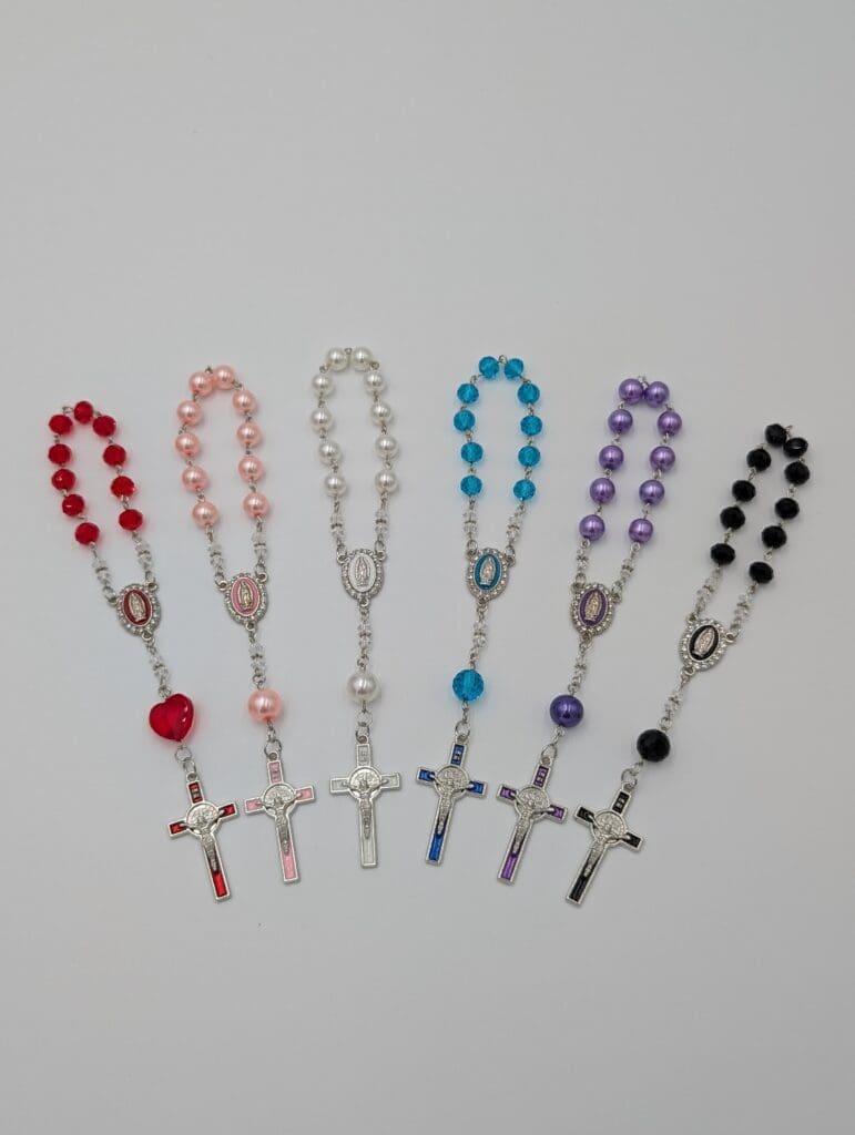 A colorful collection of rosaries in red, pink, white, blue, purple, and black showing how to pray the rosary with different bead styles